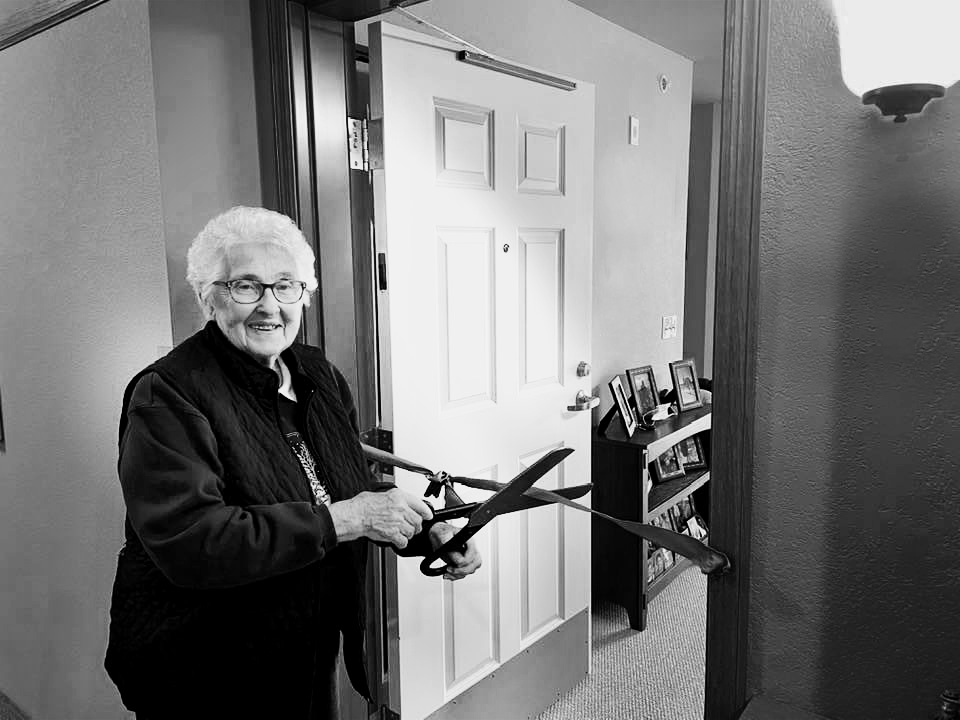 A new senior resident cutting ribbon to doorway of new apartment on move-in day.