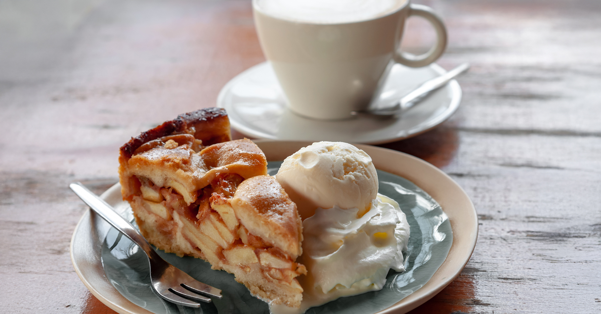 a slice of apple pie with coffee and a scoop of ice cream on a plate in a warmly lit room